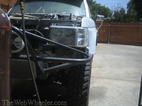 1990 Ford Bronco - Front view of a lifted off-road truck stripped to its headlights with a tube bumper, parked on concrete by a fence.