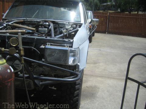 1990 Ford Bronco - Front quarter view of a white project truck with hood up, exposed engine bay, tube bumper and a gas cylinder nearby.