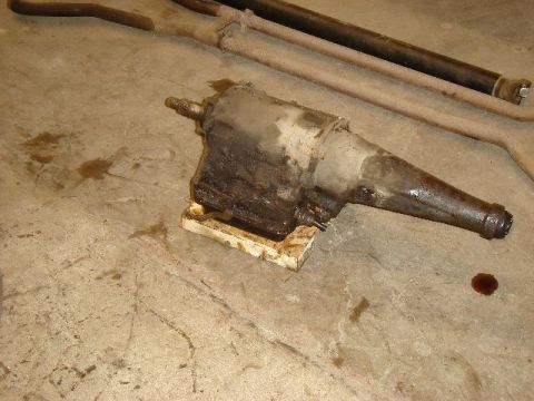 1962 Ford Thunderbird - Automatic transmission removed from a vehicle, resting on blocks with exhaust pipes nearby.