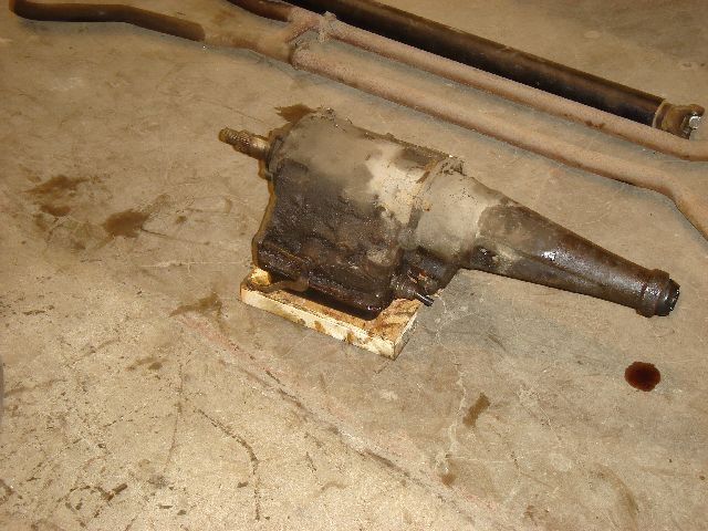 Dirty automatic transmission on wooden blocks with exhaust pipes in background