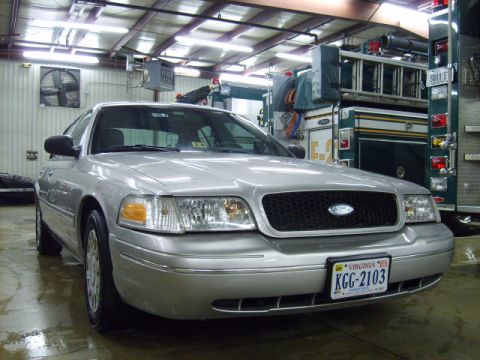 2004 Ford Crown Victoria - A silver 2004 Ford Crown Victoria is parked in a garage with fire trucks in the background.
