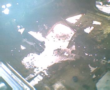 1973 Ford Ranchero - Close-up of a heavily rusted vehicle floor pan, showing significant damage and debris.