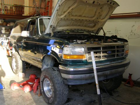 1993 Ford Bronco - A green 1993 Ford Bronco is parked in a garage with its hood open, revealing the engine bay.