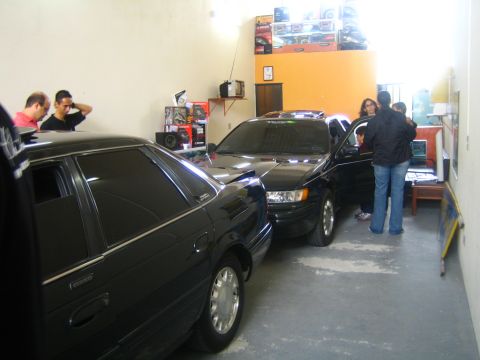 1995 Ford Taurus - Two dark sedans are parked in a garage, with people standing around the car on the right.