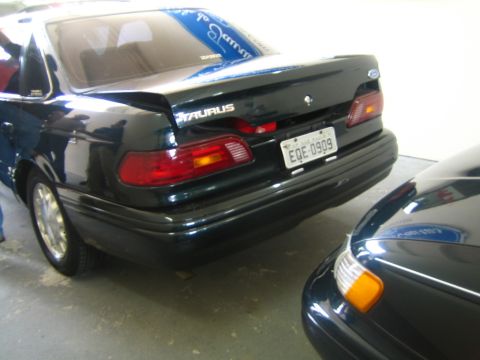 1995 Ford Taurus - A dark green 1995 Ford Taurus sedan is parked next to another dark vehicle.