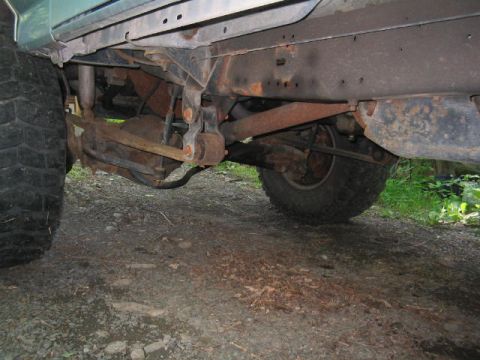 1979 Ford Bronco - Underside view of a lifted 4x4 showing the front axle, leaf spring, steering linkage, and driveline components, all coated in surface rust…