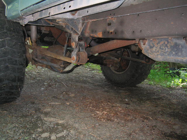 Rusty undercarriage of a lifted 4x4 showing front axle, springs and mud tires