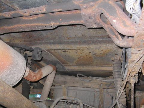1979 Ford Bronco - Underbody view of a vehicle showing heavily rusted frame rails, crossmember, exhaust piping and floor pan. A rubber exhaust hanger, coil sp…
