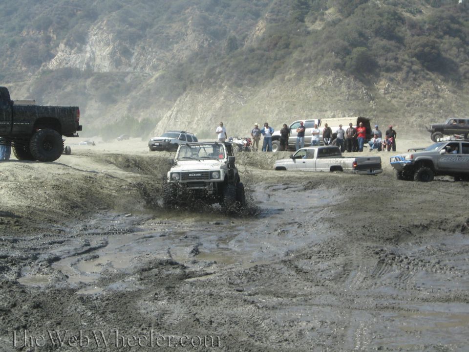 White off-road vehicle splashing mud, front view. Modified with large tires and roll cage