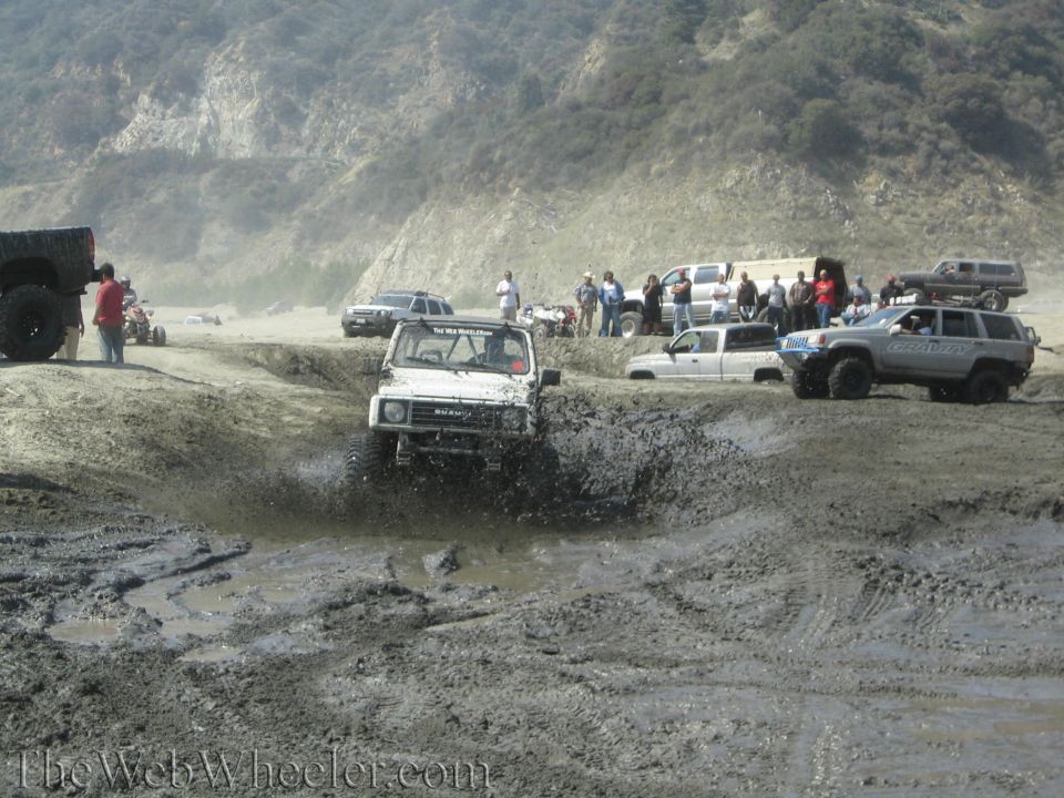 1987 Suzuki Samurai splashing through mud pit with other vehicles and people watching