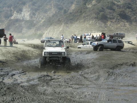 1987 Suzuki Samurai - A group of off-road vehicles navigate a muddy terrain, with a Suzuki Samurai prominently featured in the foreground.