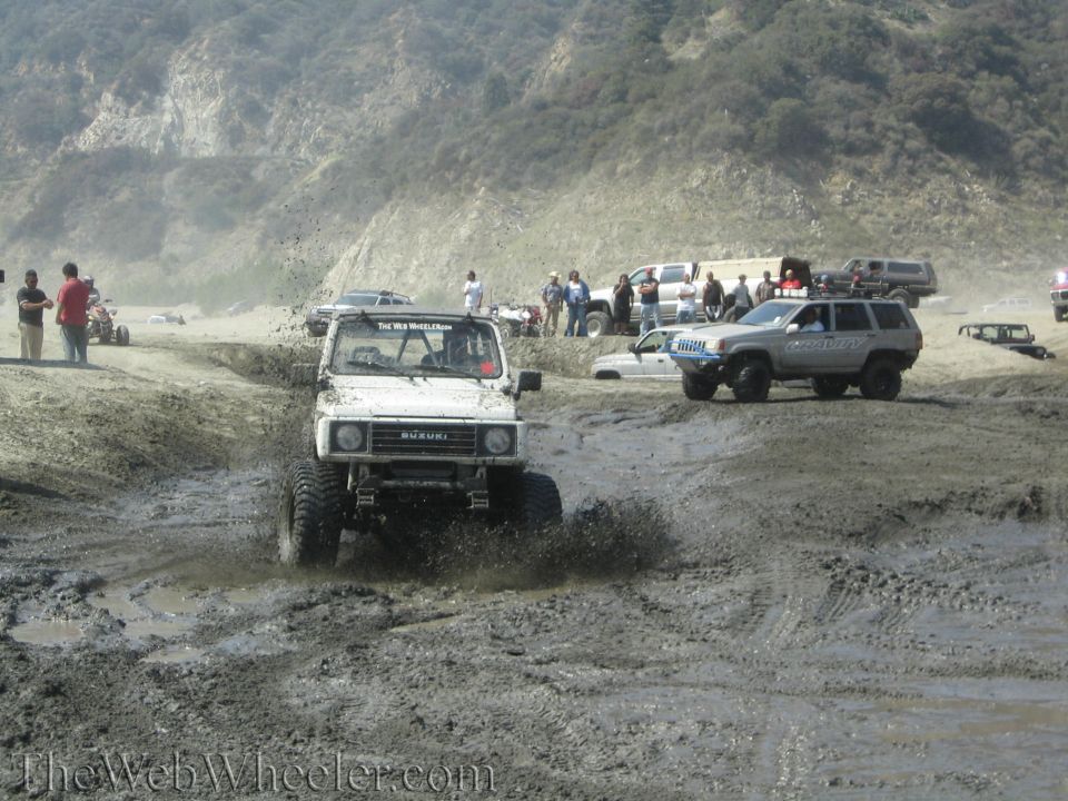 White 1987 Suzuki Samurai splashing mud, front view, modified for off-roading