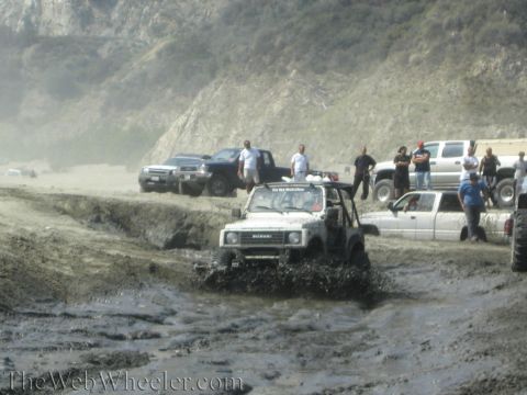 1987 Suzuki Samurai - Off-roading event with multiple vehicles navigating a muddy terrain near a coastal hillside.