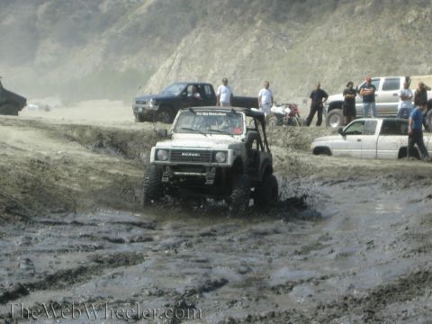 1987 Suzuki Samurai - A white Suzuki Samurai navigates a muddy terrain with other vehicles in the background.