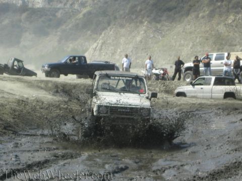 1987 Suzuki Samurai - Multiple off-road vehicles navigate a muddy terrain, with a Suzuki Samurai in the foreground.