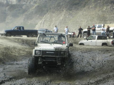 1987 Suzuki Samurai - A white 1987 Suzuki Samurai navigates a muddy off-road course with other vehicles in the background.