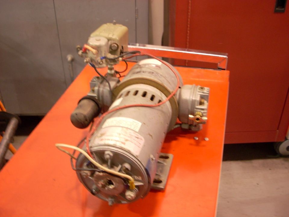 Industrial motor assembly with wiring and control box, resting on an orange surface