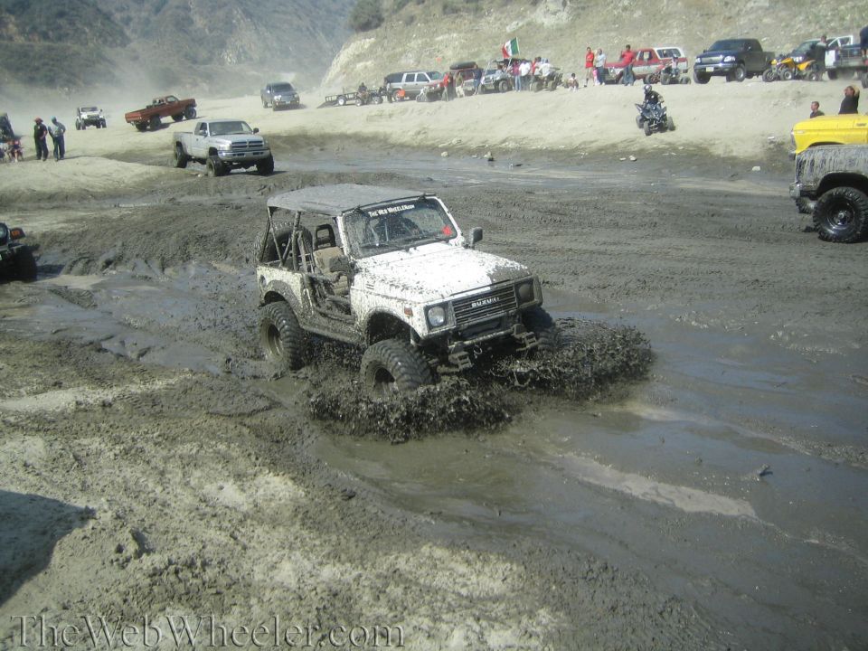 1987 Suzuki Samurai driving through mud with other vehicles in background