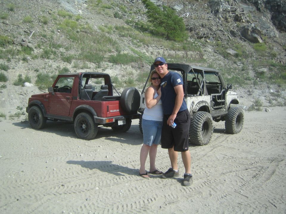 Red 1987 Suzuki Samurai parked next to a modified white Jeep with a couple standing between them