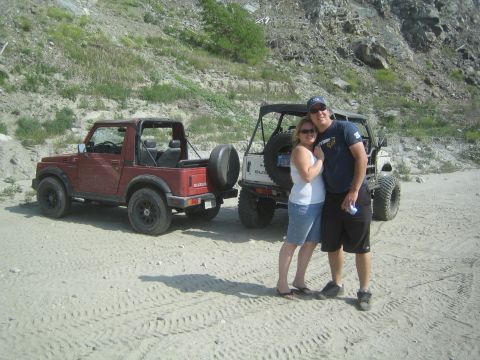 1987 Suzuki Samurai - A couple stands between two Suzuki Samurai vehicles in a sandy, outdoor setting with rocky hills in the background.