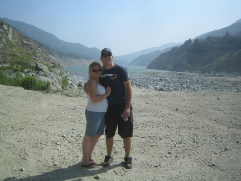 1987 Suzuki Samurai - A couple poses for a photo in a scenic outdoor location with a river and mountains.