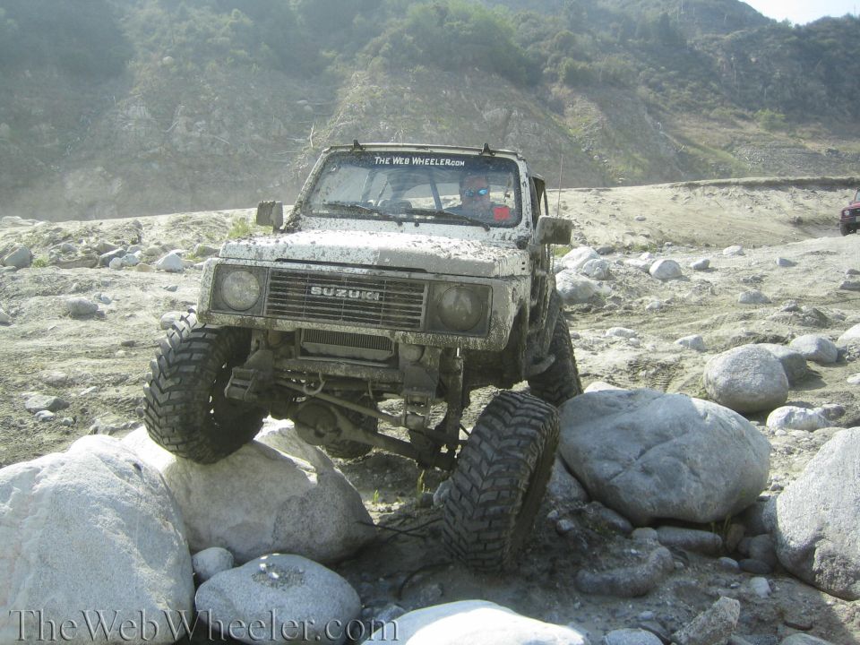 White 1987 Suzuki Samurai climbing over rocks on a dirt trail