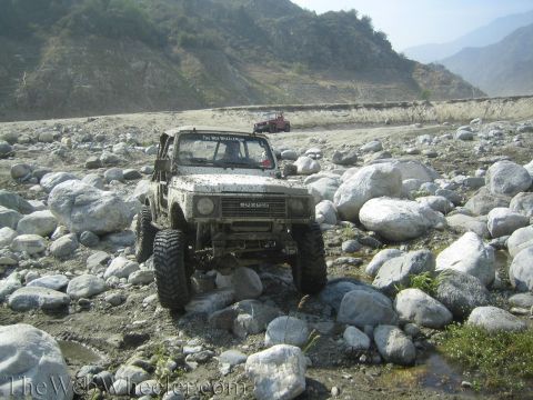 1987 Suzuki Samurai - A Suzuki Samurai navigates a rocky terrain, with another vehicle visible in the distance.