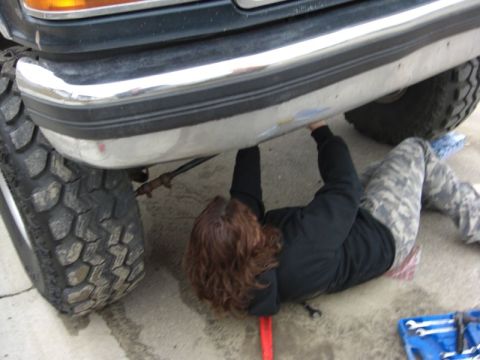 1995 Ford Bronco - A person works on the undercarriage of a large truck, with the front bumper and tires in view.