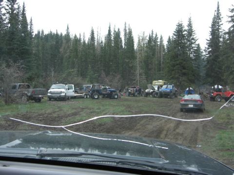 1995 Ford Bronco - A collection of off-road vehicles and a sedan are gathered in a muddy, wooded area, suggesting an outdoor recreational event.