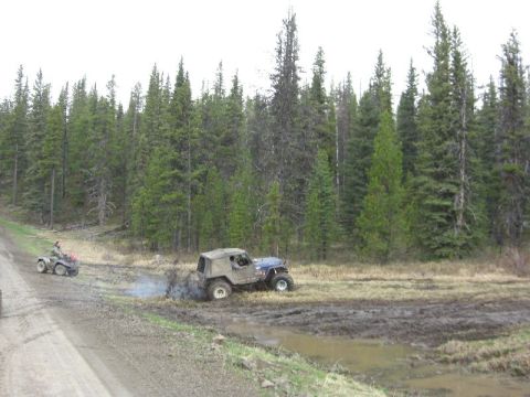 1995 Ford Bronco - Two off-road vehicles navigate a muddy trail through a forest.