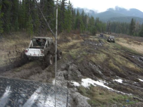 1995 Ford Bronco - Multiple off-road vehicles traverse a challenging muddy incline under a cloudy sky.