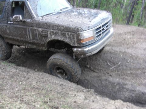 1995 Ford Bronco - A heavily mud-caked 1992 Ford Bronco navigates a challenging off-road terrain.