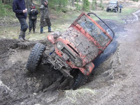 1995 Ford Bronco - An off-road vehicle is stuck in a muddy ditch, with onlookers observing the situation.