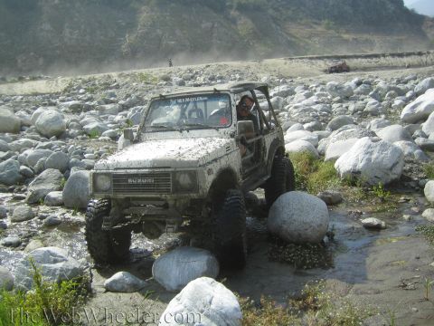 1987 Suzuki Samurai - A white 1987 Suzuki Samurai navigates a rocky riverbed, with another vehicle visible in the background.