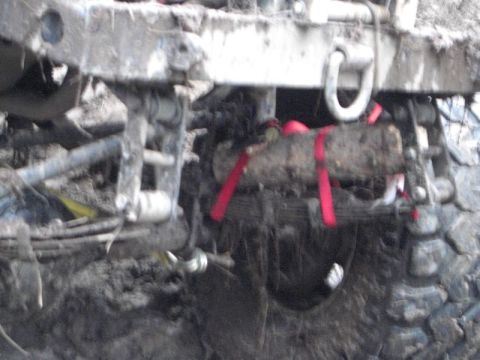 1995 Ford Bronco - The rear axle and suspension components are heavily coated in mud, with red tow straps securing a log.