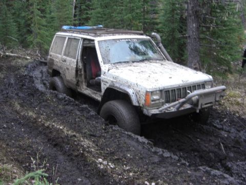 1995 Ford Bronco - Off-road Jeep Cherokee is stuck deep in mud on a wooded trail.
