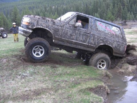 1995 Ford Bronco - This SUV is deep in the mud, with one wheel submerged in water. Another vehicle is parked nearby.