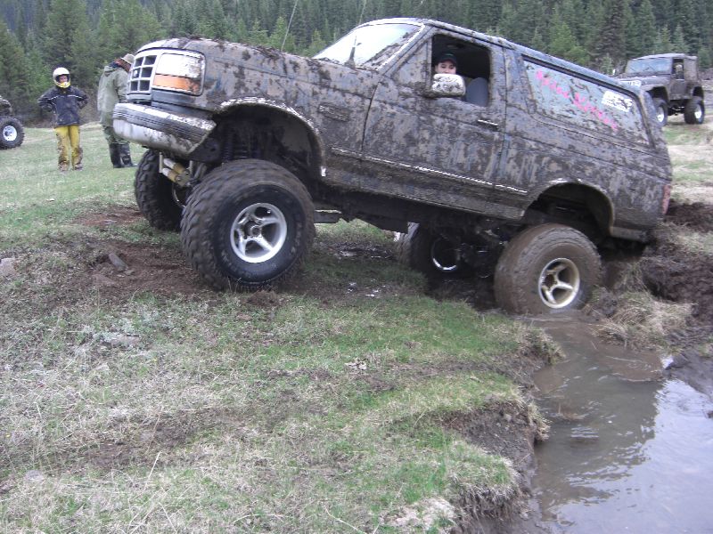 Mud-covered SUV with lifted suspension and large tires navigating a muddy ditch