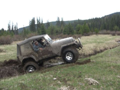 1995 Ford Bronco - Off-road vehicle stuck in mud and water, driver visible inside.