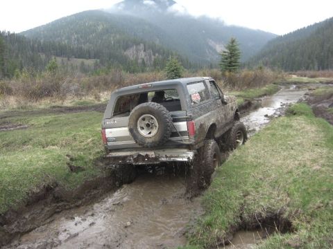 1995 Ford Bronco - A Ford Bronco navigates a muddy off-road trail in a mountainous, wooded area.