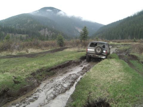 1995 Ford Bronco - A 1995 Ford Bronco navigates a muddy trail in a mountainous, wooded area.