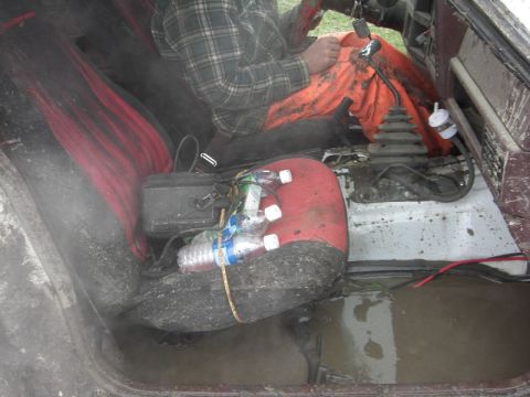 1995 Ford Bronco - The interior of a dirty vehicle shows red and black seats, a driver, and a muddy floor with standing water.