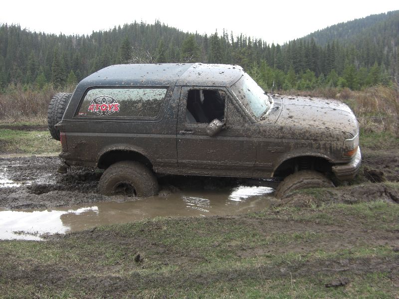 Muddy 1995 Ford Bronco stuck in a mud pit with trees in the background