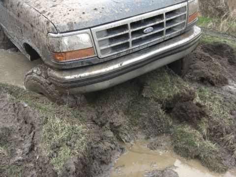 1995 Ford Bronco - A muddy Ford Bronco navigates a difficult off-road terrain, with its front tire deep in the mire.