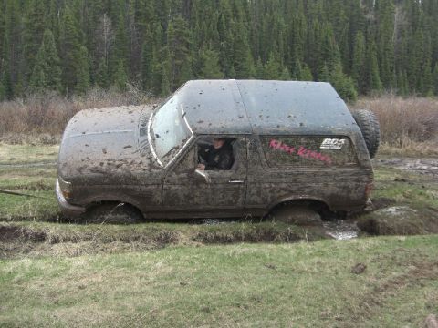 1995 Ford Bronco - Mud-covered 1995 Ford Bronco stuck deep in a muddy ditch off-road.