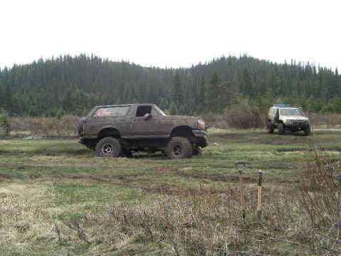 1995 Ford Bronco - A muddy 1995 Ford Bronco navigates a wet, grassy terrain with another SUV in the background.