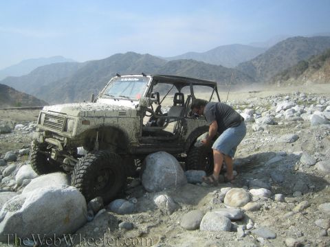 1987 Suzuki Samurai - Suzuki Samurai navigating a challenging rocky terrain, with a person attending to the front wheel.