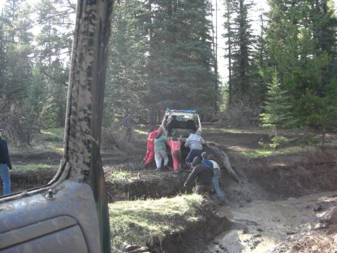 1995 Ford Bronco - A group of people work together to free a white SUV that is stuck in a muddy ditch.