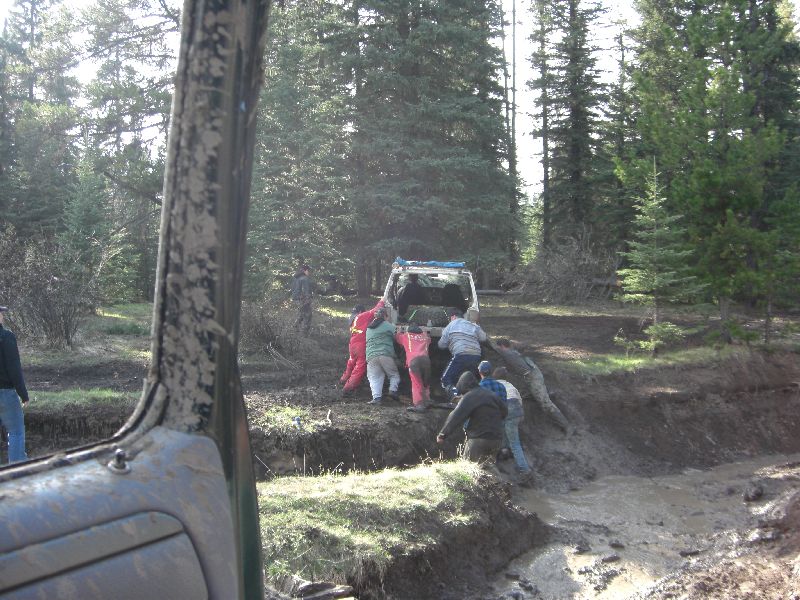 White SUV stuck in mud, people pushing it out