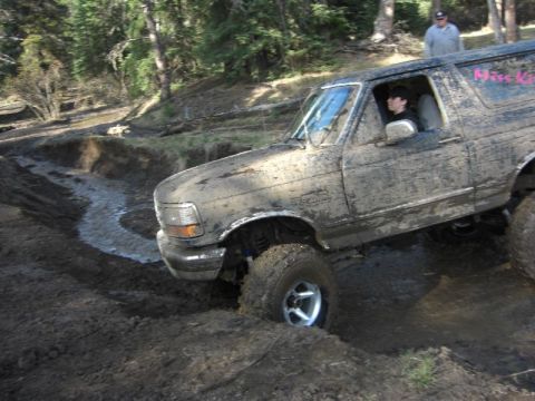 1995 Ford Bronco - This 1995 Ford Bronco is navigating a challenging muddy terrain, with one wheel deep in the mire.